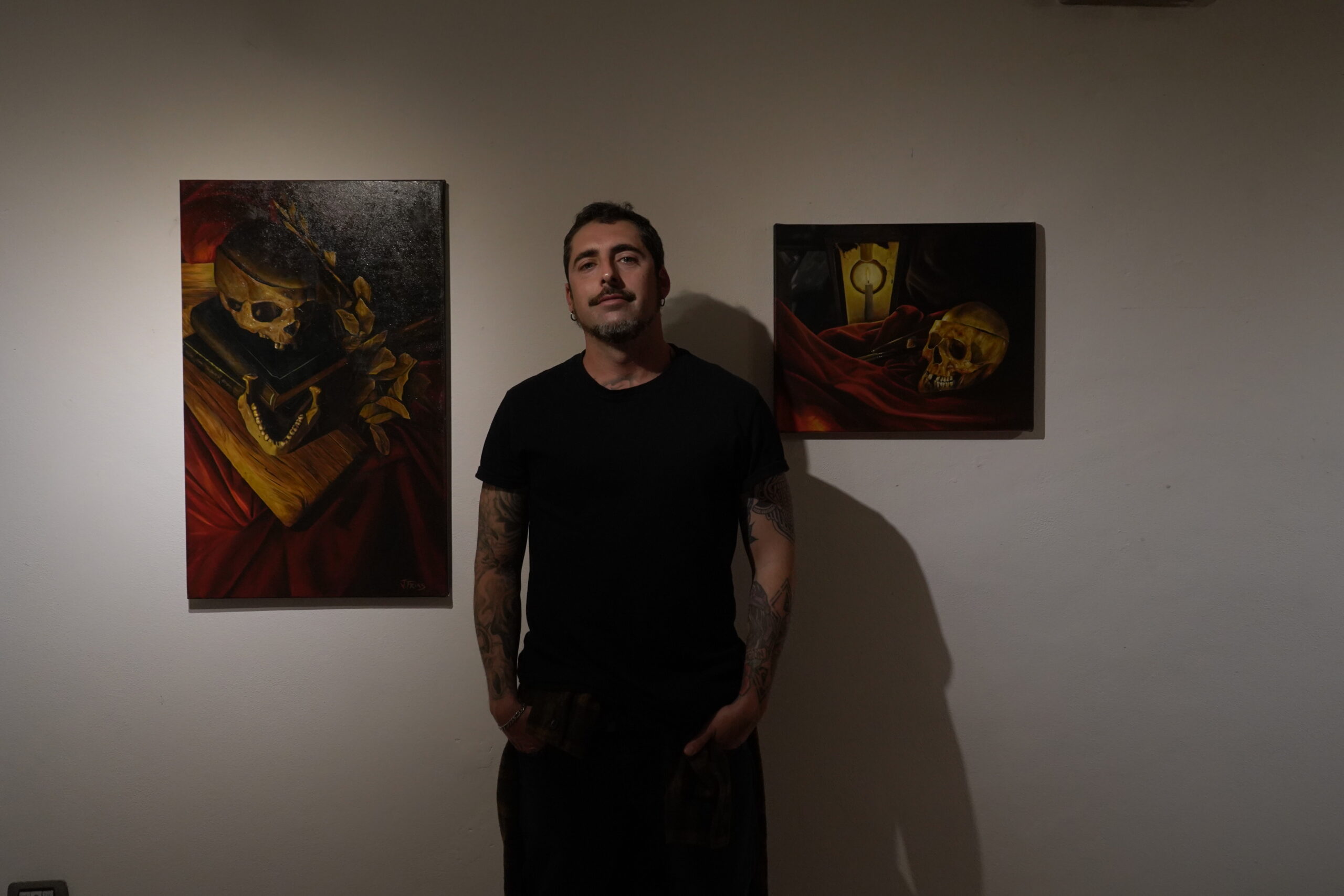 Juano Frías in his studio, standing beside two of his oil paintings